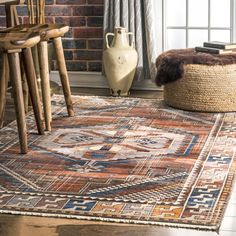 an area rug is shown in front of a brick wall and wooden chairs, with a basket on the floor next to it