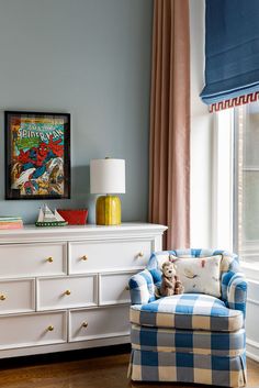 a blue and white checkered chair in front of a window with a comic cover on the wall