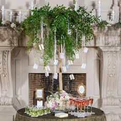 a table topped with lots of wine glasses next to a fire place covered in greenery