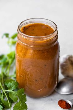 a jar filled with sauce next to some herbs