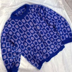 a blue knitted sweater laying on top of a white sheet