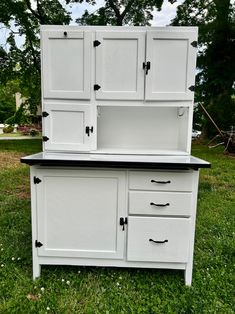 an old dresser is painted white and has black knobs on the doors, drawers, and shelves