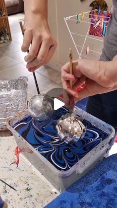 two people are working on something in a box with blue and silver paint splattered all over it