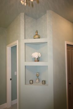 a white shelf with vases and candles on it in a room that is painted light blue