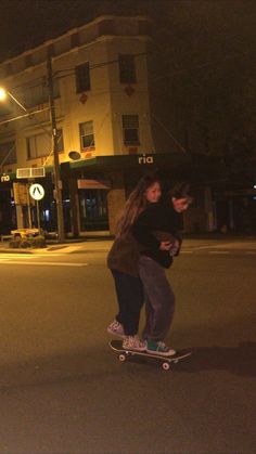 two people riding skateboards down the street at night in front of an apartment building