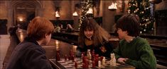 three children are playing chess in a bar with christmas lights on the wall behind them