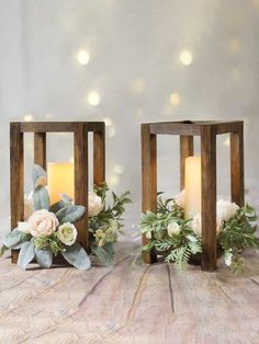 two small wooden lanterns with flowers and greenery on the sides, one is lit