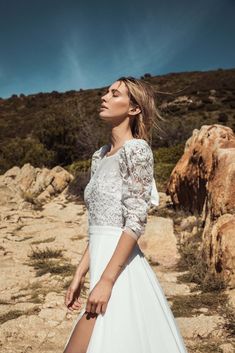 a woman in a white dress is standing on rocks and looking off into the distance