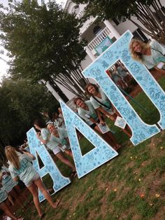 a group of young women standing next to each other in front of a large letter