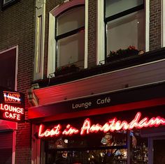 a red neon sign that reads lounge cafe in front of a brick building at night