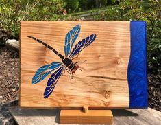 a wooden plaque with a blue dragonfly painted on it's front and back