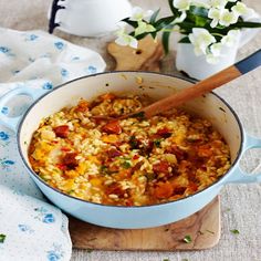 a pot filled with rice and vegetables on top of a wooden cutting board next to flowers