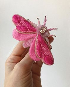 a hand holding a pink and white butterfly ornament on it's side