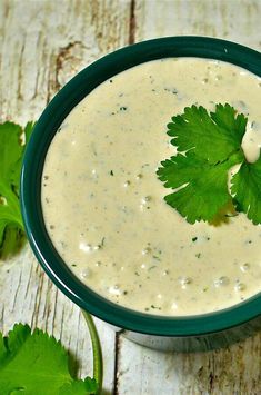 a green bowl filled with white sauce and garnished with cilantro leaves