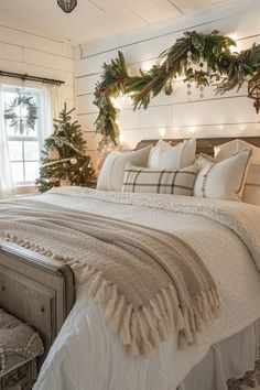 a white bed topped with lots of pillows next to a window covered in christmas wreaths