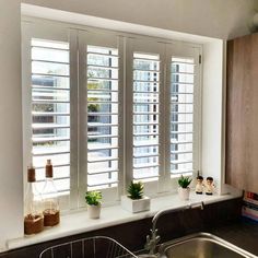 a kitchen window with white shutters and potted plants