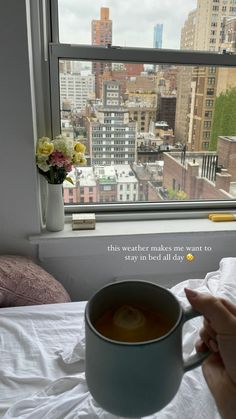 a cup of coffee sitting on top of a bed next to a window