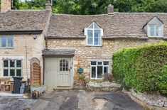 an old stone house with white windows and doors on the outside, surrounded by greenery