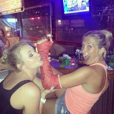 two women holding up a large piece of meat in front of a tv screen at a bar