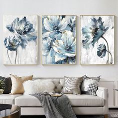 three blue and white flowers are hanging on the wall in this living room, along with pillows