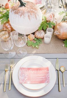 a table set with white plates and silverware, gold cutlery, pumpkin place setting