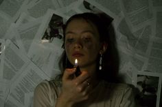 a woman holding a lit candle in her hand while laying on the floor covered with newspapers