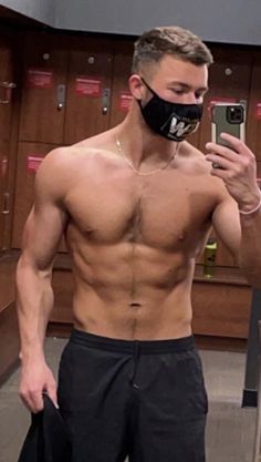 a shirtless man taking a selfie in front of lockers with his cell phone