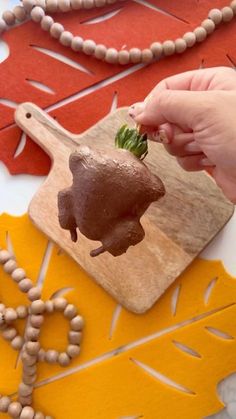 a person holding a piece of food in front of a wooden cutting board with leaves on it