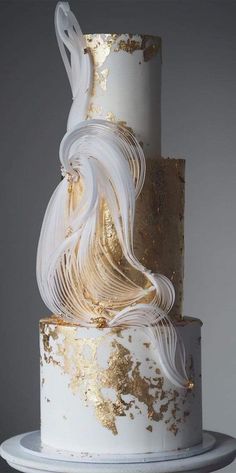 a white and gold wedding cake with swirly icing on the top, sitting on a plate