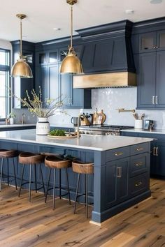 a large kitchen with blue cabinets and gold pendant lights hanging from the ceiling, along with bar stools