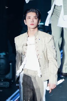 a male model in a white shirt and brown pants on the catwalk at a fashion show