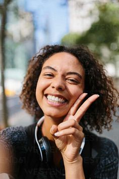 a woman making the peace sign with her hand while wearing headphones by an urban street