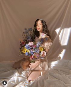 a woman sitting on top of a bed holding a bouquet of flowers in her hands