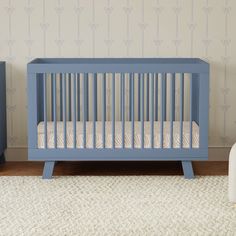 a blue crib in the corner of a room with a white rug and wallpaper