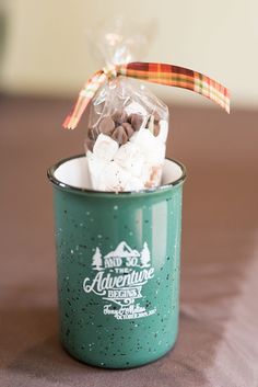 a green cup filled with marshmallows on top of a wooden table next to a bag