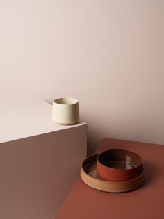 a bowl and plate sitting on top of a table next to a wall with a vase