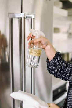 a woman is holding a bottle of wine in front of a stainless steel freezer