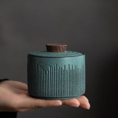 a hand holding a green ceramic container with a wooden cap on it's top