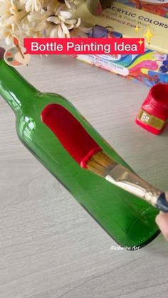 someone is painting the bottom of a green bottle with red paint and a flower in it