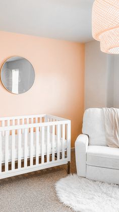 a baby's room with a white crib, chair and round mirror on the wall