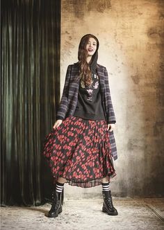 a woman standing in front of a curtain wearing a black top and red floral skirt