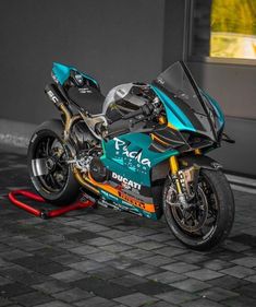 a blue motorcycle parked on top of a brick floor next to a building with windows