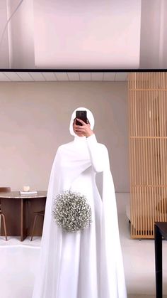 a woman dressed in white taking a selfie with her cell phone while wearing a veil