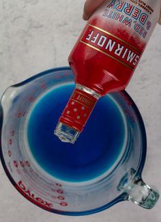 a person is holding a red and blue bottle in the air above a glass bowl