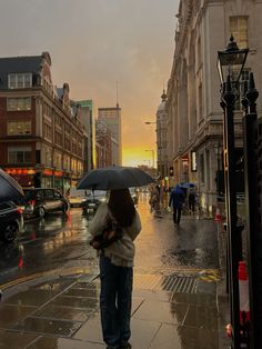 a woman holding an umbrella while standing on a wet sidewalk in the city at sunset