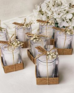 small glass candles tied with twine and some white flowers in the center are sitting on a table