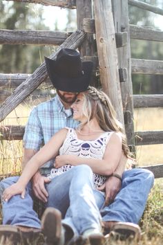 a man and woman sitting next to each other in front of a wooden fence wearing cowboy hats