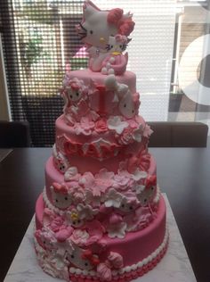 a hello kitty cake with pink frosting and white flowers on the bottom tier, sitting on a table in front of a window