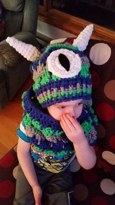 a little boy wearing a knitted hat and scarf with an eyeball on it