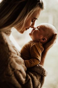 a woman holding a baby in her arms and kissing it's face with the other hand